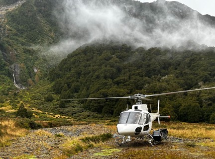 A landed helicopter sitting atop a clouded mountain.